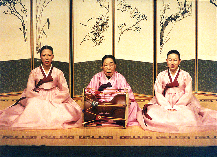 (esq. para dir.) Yu Ji Sook, Oh Bok Byeo e Kim Gwang Sook. Foto das 3 mestres de Seodo Sori citadasno blog. Todas vestindo roupas tradicionais coreanas (hanbok) em um teatro com um cenário tradicional antigo de telas de divisão de bambu e pinturas de galhos e gramas. Estão sentada lado a lado. À esquerda está Yu Ji Sook, no centro está Oh Bok Nyeo segurando um janggu (tambor coreano), à direita está Kim Gwang Sook. Todas usam hanbok de tecido de seda rosa claro com detalhes em vinho.